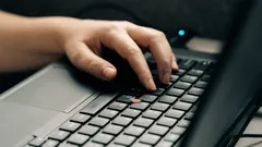 Osoba pracující na černém a šedém laptopu doma